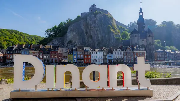 Dinant, Namur, Wallonia, Belçika. 6 Haziran 2024. Dinant tabelasıyla şehir manzarası, kayalık dağın tepesinde kale, Meryem Ana 'nın kolej kilisesi, binalar ve Meuse nehri, güneşli yaz günü.