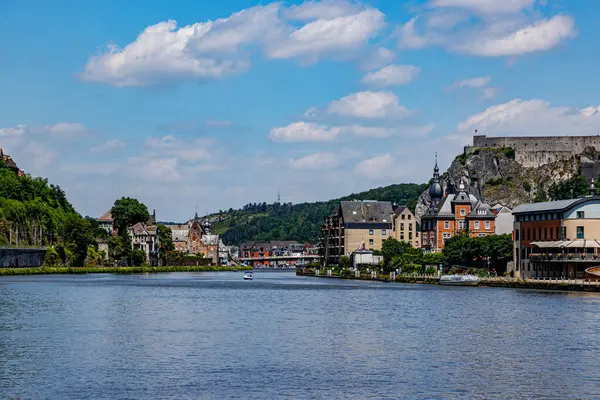 stock image View of Meuse river with cityscape of Dinant resort town and citadel on top of rocky mountain against blue sky in background, lush trees on hill, sunny summer day in Namur province, Wallonia, Belgium