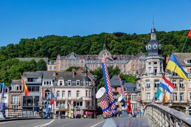 Dinant, Namur, Wallonia, Belçika. 5 Haziran 2024. Dinant 'taki Avrupa ülkelerinin saksafon ve bayrak heykelleri, binalar ve Notre-Dame De Bellevue Lisesi' nin arka planında yer alan köprü