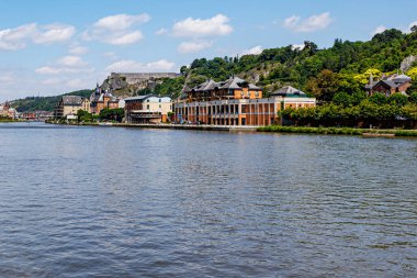 Arka planda tatil köyü manzaralı Meuse nehri kayalık dağın tepesinde kale ve Belçika 'nın Valonya eyaletinin Namur ilçesinde güneşli bir yaz günü olan Dinant Hanımefendisinin kolej kilisesinin kuleleri.