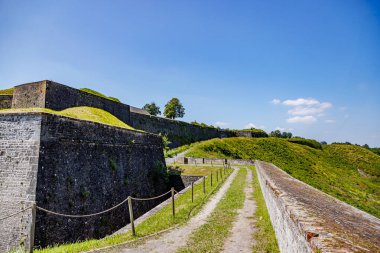 Tepedeki Charlemont Kalesi 'nin dışındaki kirli yol. Kompleksin etrafını saran büyük, kalın taş duvarlar. Arka planda mavi gökyüzü.