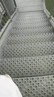 Spor ayakkabılı bir erkek bacağının gözlem kulesinde metal merdivenlerden inişi, parmaklıklı metal bir yapı, üst açı perspektifi. Dikey video
