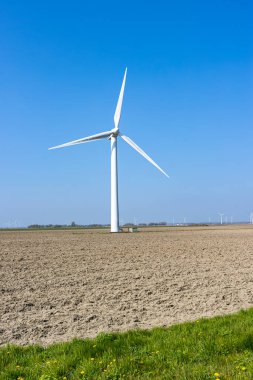 Hollanda tarlalarında büyük rüzgar türbini, yenilenebilir elektrik, kuru arazi, arka planda yel değirmenleri ve ağaçlar, Kuzey Hollanda 'da mavi gökyüzü ile güneşli bir gün.