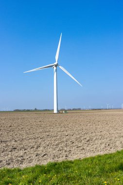 Hollanda tarlalarında büyük rüzgar türbini, yenilenebilir elektrik, kuru arazi, arka planda yel değirmenleri ve ağaçlar, Kuzey Hollanda 'da mavi gökyüzü ile güneşli bir gün.