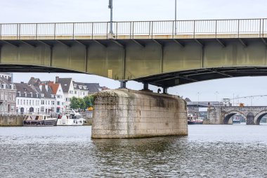 Wilhelminabrug Köprüsü 'nün metal destekli beton üssü, arka planda Sint Servaasbrug köprüsü ve şehir manzarası, sakin su, Hollanda' nın güney Limburg kentinde bulutlu bir gün
