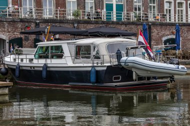 Maastricht şehrinin eski tarihi iç limanının rıhtımında demirli asma şamandıraları ve Hollanda bayrağı olan teknenin yan görüntüsü, arka planda bina, Güney Limburg, Hollanda 'da bulutlu bir gün.