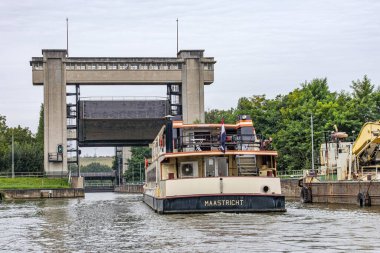 Fare nehri üzerinden Bosscherveld 'e doğru giden turist teknesi, Zuid-Willems kanalı, arka planda gri gökyüzüne karşı yeşil yapraklı ağaçlar, Maastricht, Güney Limburg, Hollanda' da bulutlu bir gün