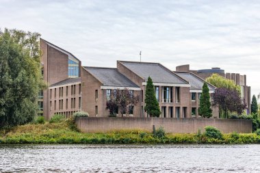 Gouvernement aan de Maas bir hükümet binası, Meuse nehrinin üzerindeki bir ada, yapraklı ağaçlarla çevrili, Maastricht, Güney Limburg, Hollanda 'da bulutlu bir gün.