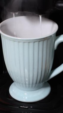 Elektrikli kahve makinesinin içindeki fincana süt damlatırken çekilen statik pozu, lezzetli macchiato kahvesi yapıyor. Lezzetli ev yapımı içecek kavramı. Dikey video