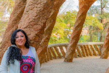 Yüzünde gülümseme olan tombul bir turist, taş sütunlar ve taş duvar, Antoni Gaudi 'nin Parc Gell' deki Bugadera Viaduct, gerçeküstü tasarım ve şekiller, Barcelona 'da güneşli bir gün, Katalonya, İspanya