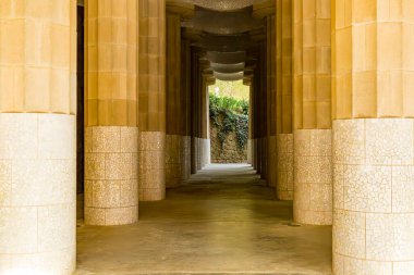 Beyaz kiremitlerle kaplı devasa flütlü sütunlar arasında düz koridor, Antoni Gaudi tarafından Parc Guell 'deki Hypostyle salonu, Katalona, İspanya' da güneşli bir gün.