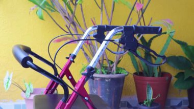 Yürüyebilecek koltuğu olan bir yürüteç kolu ve arka planda sarı duvarı olan yaşlı bir kadın. Engelli insanların günlük yaşamlarını kolaylaştıracak nesneler kavramı