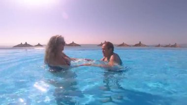 Dans hareketleriyle yaşlı bir kadın rehabilitasyonu için su ritmi. İki yaşlı kadın havuzda egzersiz yapıyor, kollarını, belini ve karnını güçlendiriyor, güneşli bir günün tadını çıkarıyor. Etkin yetişkin yaşam tarzı konsepti