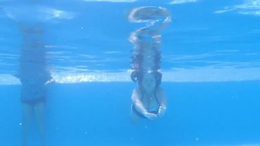 Yetişkin bir kadın havuzda yüzüyor, kollarını sallıyor ve huzur içinde yüzüyor, mavi fayanslı havuz, kristal berrak su, güneşli ve rahatlatıcı bir tatil günü. Etkin yetişkin yaşam tarzı konsepti