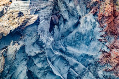 Kaya duvarının yüzeyinde pürüzlü desenlere sahip kaya oluşumunun eğimi, mavi, gri, kırmızı ve sarı renklerin birleşimi, Loreto Körfezi Ulusal Deniz Parkı 'ndaki Coronado Adası, Baja California Sur, Meksika