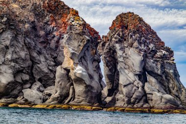 Meksika 'nın Coronado Adası kıyılarında devasa kaya oluşumları, tepesinde kahverengi renkli volkanik lav kayaları olan yamaçlar, Baja California Sur, Meksika' daki Loreto Körfezi Ulusal Deniz Parkı 'nda bulutlu bir gün.