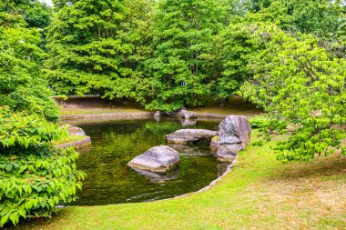 Japon halk bahçesinde büyük taşlarla çevrili ağaç çizgili manzara, arka planda yemyeşil ağaçlar, Hasselt, Belçika 'da bulutlu bir gün
