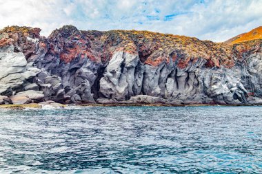 Coronado Adası 'ndaki kayalık dağlarla Meksika kıyı manzarası, volkanik lav oluşumları, tepesinde gri yamaç ve kahverengi, Baja California Sur, Meksika' daki Ulusal Deniz Parkı 'nda bulutlu bir gün.