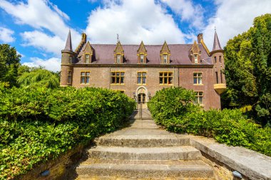 TerWormista Kalesi ön cephede, hendeğe çıkan merdivenler, tuğla duvarlar, iki yan kuleler ve çatılı çatı, yapraklı ağaçlarla çevrili, Heerlen, Güney Limburg, Hollanda 'da güneşli bir gün.