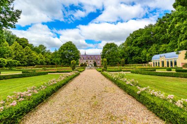 Yeşil çalılar ve beyaz çiçekler arasındaki düz yol halka açık park manzarası TerWorm Kalesi ve arka planda yapraklı ağaçlar Heerlen, Güney Limburg, Hollanda 'da güneşli bir bahar günü
