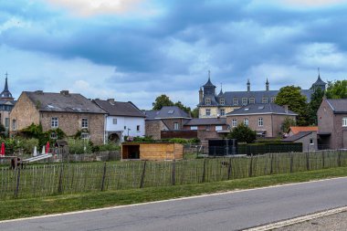 Bahçeler, tarım bahçeleri, kır yolları ve arka planda fırtınalı gökyüzüne karşı gri arka planda kalesi olan tuğla evler, Oud-Rekem, Limburg, Belçika 'nın varoşlarında bulutlu bir gün