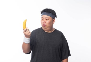 Young Asian funny fat sport man holding banana isolated on white background. Healthy lifestyle concept. clipart
