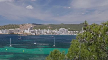 Deniz, ağaçlar, dağlar, yatlar ve turkuaz suda yüzen bir teknenin olduğu bir otelin balkonundan manzara. İbiza, İspanya