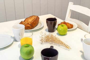 Fresh tasty breakfast served on a white table with croissants, apples and orange juice
