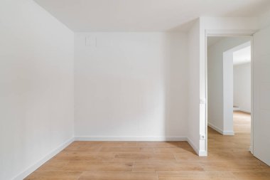 Empty room with laminate flooring and newly painted white wall in refurbished apartment with corridor leading to other rooms. Repair and construction concept