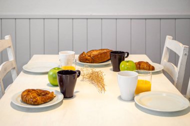 Fresh tasty breakfast served on a white table with croissants, apples and orange juice