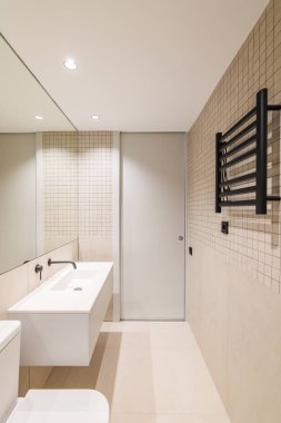 Modern banyo, bej fayanslar, siyah radyatör ve beyaz lavabo..