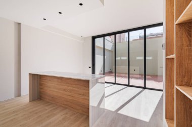 Yenilenmiş bir dairenin içi boş ve büyük pencerelerden içeri güneş ışığı giriyor. Ada ve ahşap mobilyalı modern mutfak.