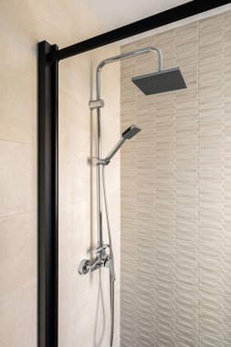 Black shower and ceramic tiled wall. Vertical view of modern minimalist interior of beige color.