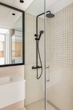 Bej kaplama banyoda modern duş bölgesi. Siyah yağmur başlığı, el ele tutuşan duş ve cam bölme