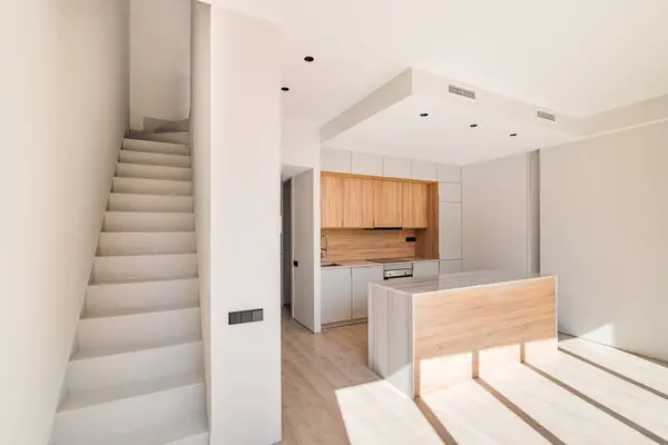 Empty interior of refurbished duplex with stairs and modern kitchen with island and wooden furniture.