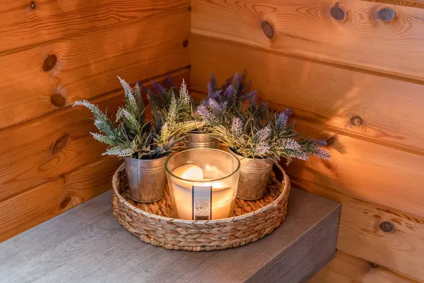 Burning candle in glass candlestick with plants as a decor in a bathroom with wooden walls.