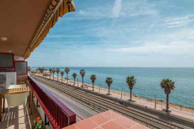 Embankment and ocean water view from hotel terrace in Vilassar de Mar. Picturesque sea waterfront with palms and railroad under blue sky clipart