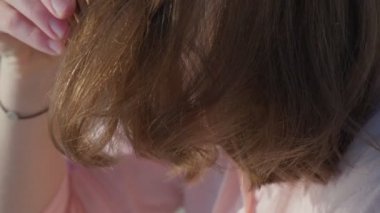 Kahverengi saçlı genç bir kadın. Saçının uçlarını tarıyor. Geniş dişli taraklı. Kadın turist, hafta sonu boyunca kumlu sahil şeridinde oturarak plaj kenarı kaçamağından hoşlanıyor.