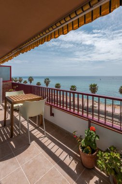 Shady terrace with table and potted plants by sea beach in Vilassar de Mar. Comfortable place to rest in tourist apartment at Catalonia resort clipart