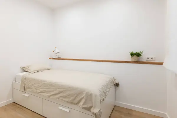 High single bed with drawers for storing linen against the background of a shelf with indoor plants and a white wall. Concept of a new minimalist renovation in the apartment of a lonely person.