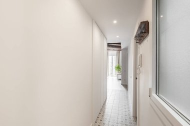 Uzun, parlak bir koridorun yatay görüntüsü. Giriş kapısı ve oturma odası manzarası. Genç bir aile tarafından satın alınan bir apartmanın zeminden tavana penceresi var. Metin için yer.