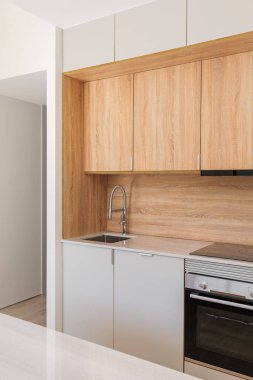 Duvar boyunca hafif ahşap dolapları olan modern bir mutfak var. Mermer üst entegre indüksiyon hob ve lavabo