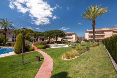 Yeşil budanmış ağaçlar, temiz çimenler, temiz suyla küçük havuzlar ve ılık yaz havasında akşam yürüyüşleri için yürüyüş yolları olan yerleşim yerindeki otel kompleksinin içindeki bakımlı mini park.