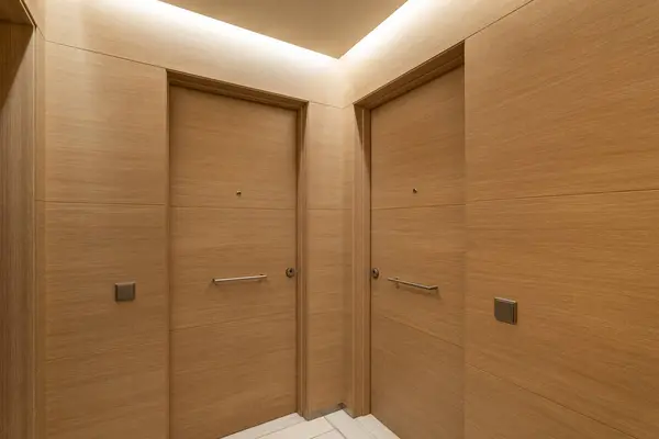 Soft light from niche under ceiling illuminates doors and walls in common corridor. Interior is made in same style of precious wood. Entrance doors are equipped with bell and door peephole
