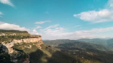 Dağlık yeşil bir vadide mavi gündüz vakti bulutların hareket hızını hızlandıran bir çekim. Bulutların gölgesi bir dağ vadisindeki kayalıklarda ve tepelerde gökyüzünde süzülüyor. Doğanın havadan görünüşü.