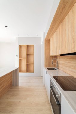 Duvar boyunca hafif ahşap dolapları olan modern bir mutfak var. Mermer kapağın tümleşik indüksiyon hob ve lavabosu var. Kapının önünde rafları mutfakla aynı tarzda olan bir raf görebilirsiniz.