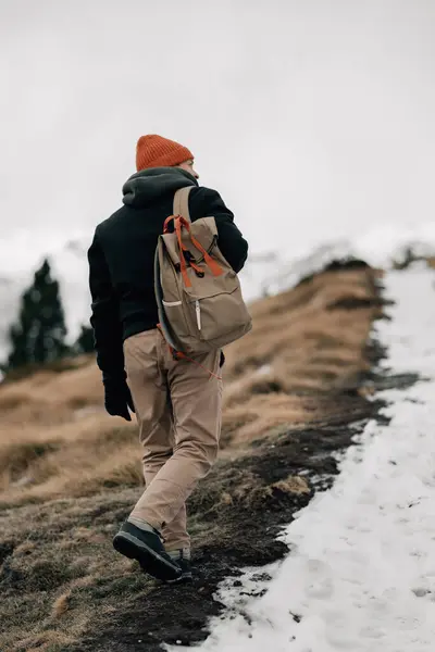 stock image A lone hiker traverses a snowy trail along the edge of a mountain, highlighting the isolation of the trek.