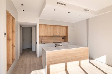 Açık modüler mutfak, dolap tasarımlı, beyaz ve açık kahverengi renklerde. Güneş ışığı yeni modern mutfak setini aydınlatıyor. Beyaz mutfak ünitesi mermer kapaklı ve ballı meşe mobilyalı.