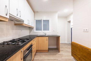 Modular furniture in kitchen with white cabinets on top of wall and cabinets with wood doors below. Black worktop with gas stove. On wall opposite, there is folding solid wood tabletop to save space clipart