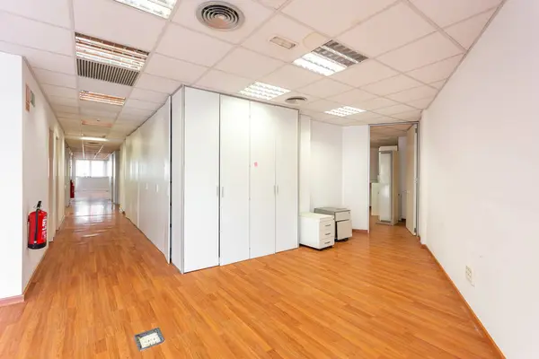 Empty abandoned room with white and wooden office lockers to store office stuff. Corner of a white wall in an office corridor with white ceiling tiles and burnt out fluorescent lamps